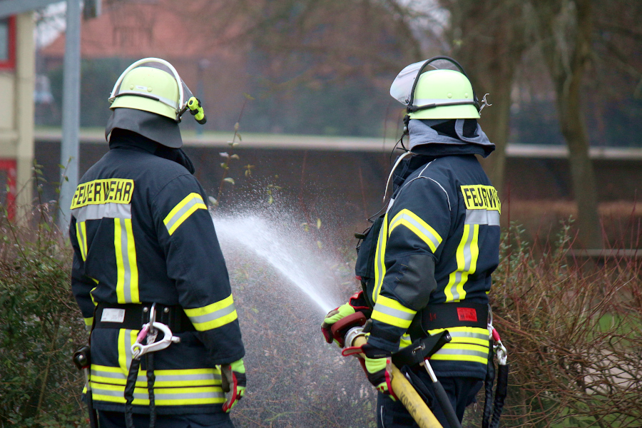 Zwei Feuerwehrleute simulieren eine sogenannte Riegelstellung, mit der verhindert werden soll, dass ein Feuer auf ein Gebäude überspringt. Foto: Thomas Dohna