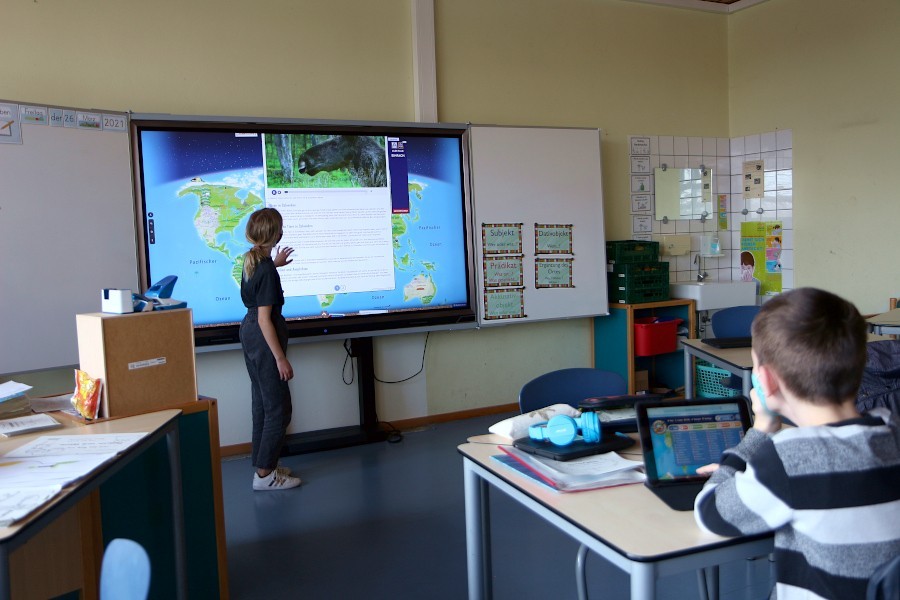 Eine Schülerin der Grundschule Asemissen steht am Smartboard in ihrem Klassenraum. Sie hat gerade von einer Lernplattform einen Beitrag zum Sachkundeunterricht aufgerufen. Der Schüler im Vordergrund sucht auf seinem Tablet einen anderen Beitrag. Foto: Thomas Dohna