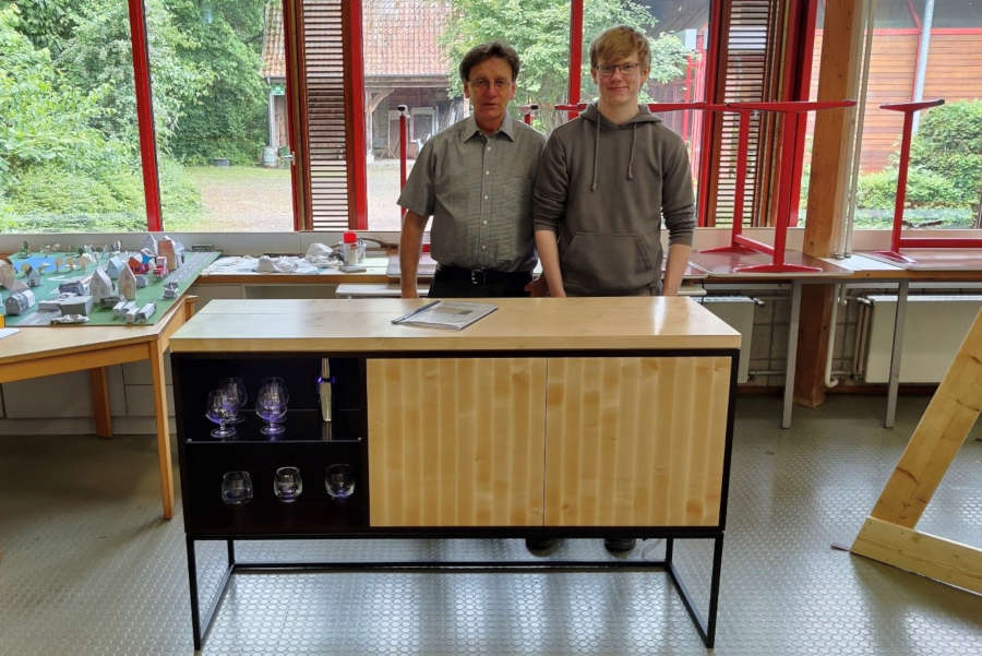 Paul Vollmer (rechts) steht mit seinem Ausbilder Horst Kesting an seinem Gesellenstück, einem Sideboard mit Hausbarfunktion. Foto: Gemeinde Leopoldshöhe