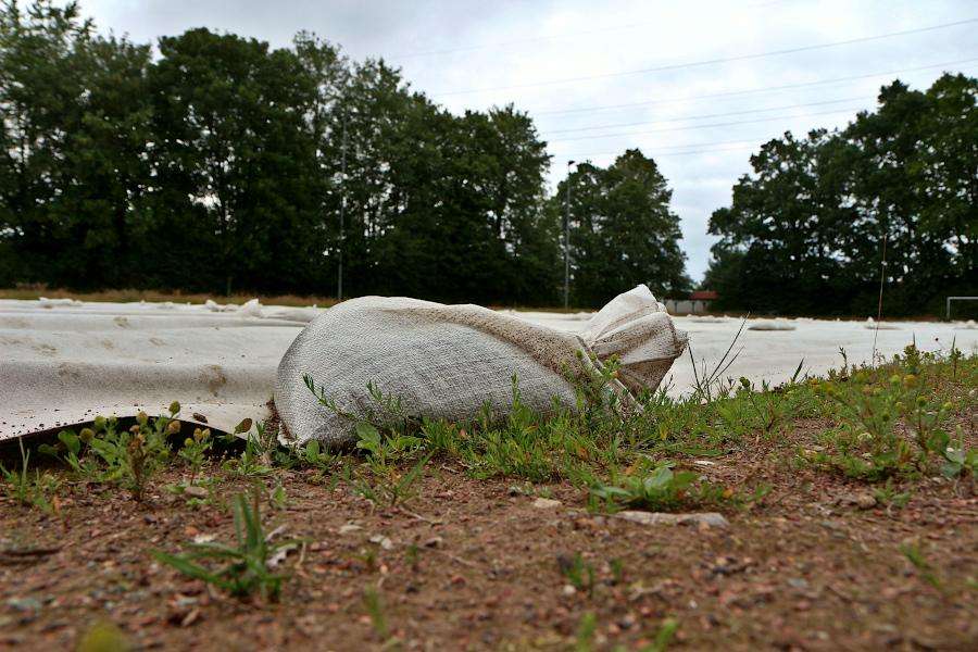 Ein Sandsack beschwert ein Vlies, das auf dem Sportplatz Greste liegt. Das Vlies soll dioxinhaltigen Staub hindern, in die Umgebung getrieben zu werden. Foto: Thomas Dohna