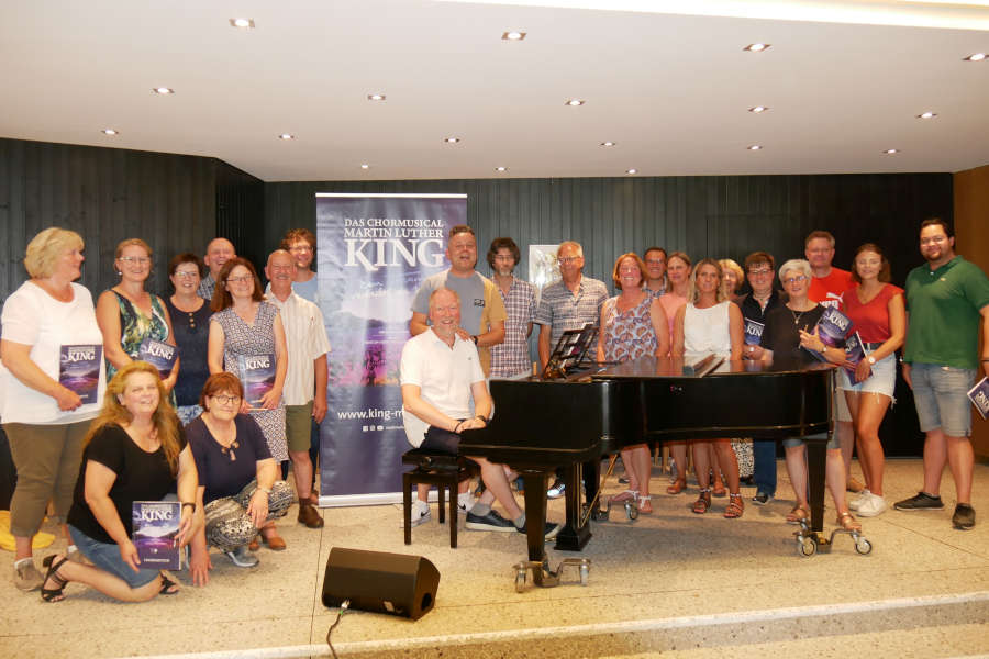 Chorleiterschulung in St. Nicolai mit Staffelübergabe. Komponist Hanjo Gäbler in der Mitte übergibt Peter Stolle am Flügel die Leitung für die Proben und Aufführungen. 23 Chorleiter aus Lippe umrunden das Geschehen