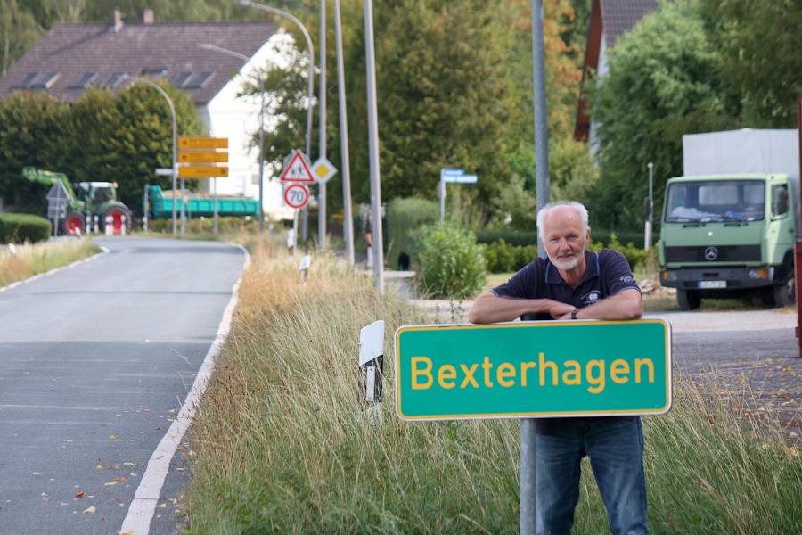 Klaus Droste steht an einem Ortshinweisschild in Bexterhagen. Im Hintergrund kreuzt die Bielefelder Straße den Alten Postweg. Droste möchte, dass Ortseingangsschilder auf den Ortsteil hinweisen und die gefahrenen Geschwindigkeiten senken. Foto: Thomas Dohna