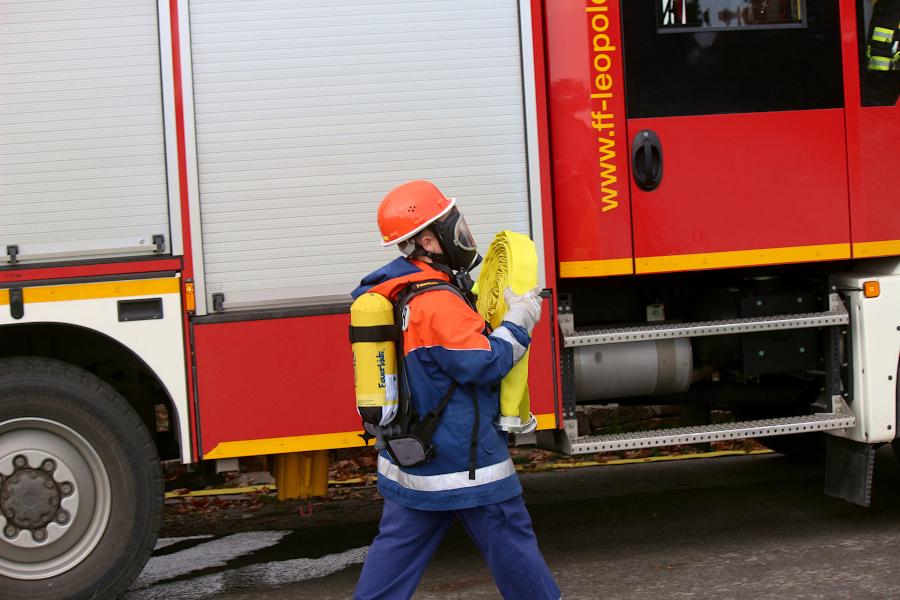 Ein Truppmann bringt einen Schlauch zur Brandstelle. Er trägt eine Maske und ein Modell eines Atemschutzgerätes auf dem Rücken. Foto: Thomas Dohna