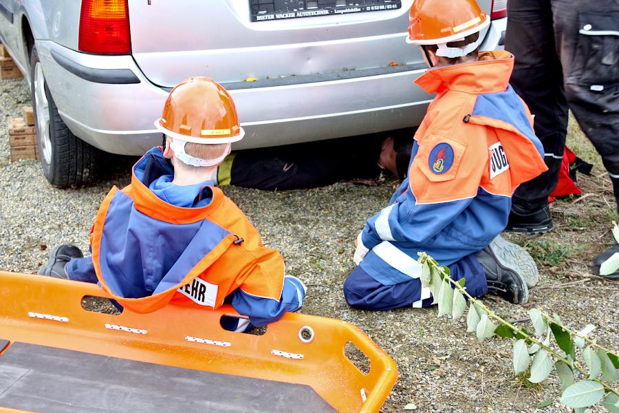 Zwei Jugendfeuerwehrleute warten darauf, dass das Auto hoch genug angehoben ist, um die Puppe, die als Unfallopfer dient, hervorziehen zu können. Foto: Thomas Dohna