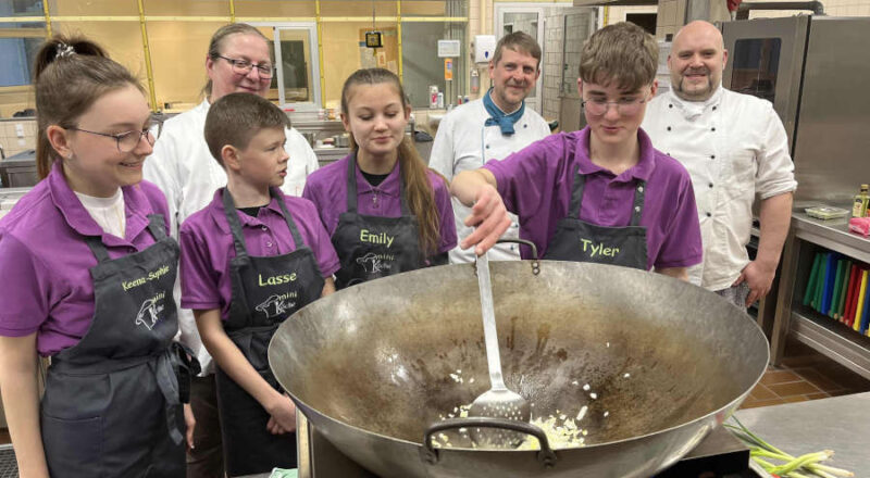 Juniorköche bei der Arbeit mit Bild Anja Limberg (obere Reihe links), Vorsitzende des Köcheclubs Lippe, Michael Schwarze (obere Reihe Mitte), Teamleiter und Köcheclub-Mitglied Juri Kracht (obere Reihe rechts). Foto: IHK Lippe