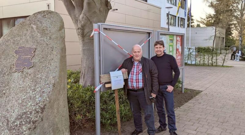 Andreas Brinkmann und Christian Kühnel (beide SPD) stehen an einem der zerstörten Schaukästen. Dort haben sie einen Briefkasten aufgestellt, in den Unzufriedene anonym ihre Anregungen einwerfen können. Foto: Brinkmann