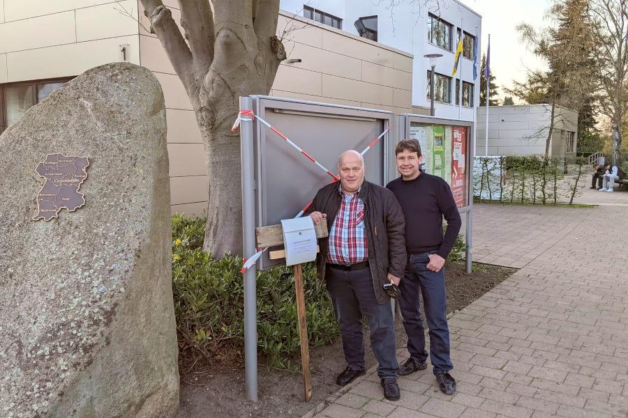 Andreas Brinkmann und Christian Kühnel (beide SPD) stehen an einem der zerstörten Schaukästen. Dort haben sie einen Briefkasten aufgestellt, in den Unzufriedene anonym ihre Anregungen einwerfen können. Foto: Brinkmann