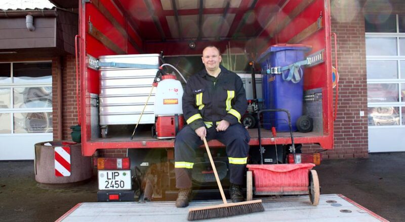 Ronny Smok sitzt auf der Ladefläche des Gerätewagens Logistik der Feuerwehr Leopoldshöhe. Links neben ihm eine Handspritze, aus dem ein flüssiges Mittel zur Ölbekämpfung auf die Straßen gespritzt werden kann. Rechts neben ihm steht der Streuroller, mit dem trockenes Ölbindemittel verteilt wird. Mit dem Besen arbeiten die Wehrleute das Mittel ein und fegen es anschließend zusammen. Das ölgetränkte Mittel kommt dann in die blaue Tonne. Foto: Thomas Dohna