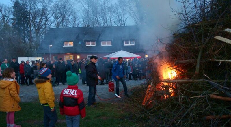 Gerd Deppe steht mit einem Brenner am Holzhaufen auf dem Gelände des TuS Asemissen. Er hat gerade das Osterfeuer angezündet. Im Hintergrund schauen viele hundert Menschen zu. Foto: Thomas Dohna