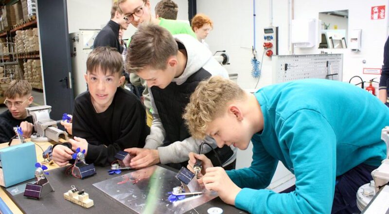 Noah, Jannis und Finn-Malte (von links) löten ein Solarmodul an einen mit einem Motor betriebenen Ventilator. Angeleitet hat sie der Mechatroniker-Auszubildende Constantin (im grünen Shirt). Die Jugendlichen waren anlässlich der Bauteilübergabe für den Solar Racing Cup bei der Firma Spilker zu Gast. Foto: Thomas Dohna