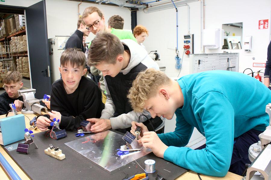 Noah, Jannis und Finn-Malte (von links) löten ein Solarmodul an einen mit einem Motor betriebenen Ventilator. Angeleitet hat sie der Mechatroniker-Auszubildende Constantin (im grünen Shirt). Die Jugendlichen waren anlässlich der Bauteilübergabe für den Solar Racing Cup bei der Firma Spilker zu Gast. Foto: Thomas Dohna