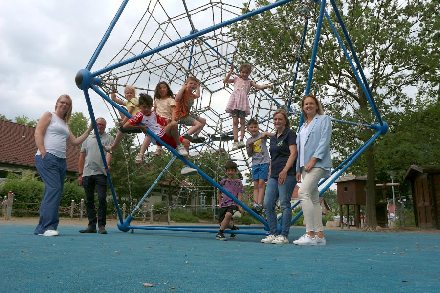 Architektin Edina Albrecht, Fachbereichsleiter Dirk Puchert-Blöbaum (beide Gemeindeverwaltung), ein Schwung Kinder der Grundschule, Sanrda Kostrz und Schulleiterin Diana Fleer stehen und sitzen in und am neuen Klettergerüst im Hof der Grundschule Asemissen. Foto: Thomas Dohna