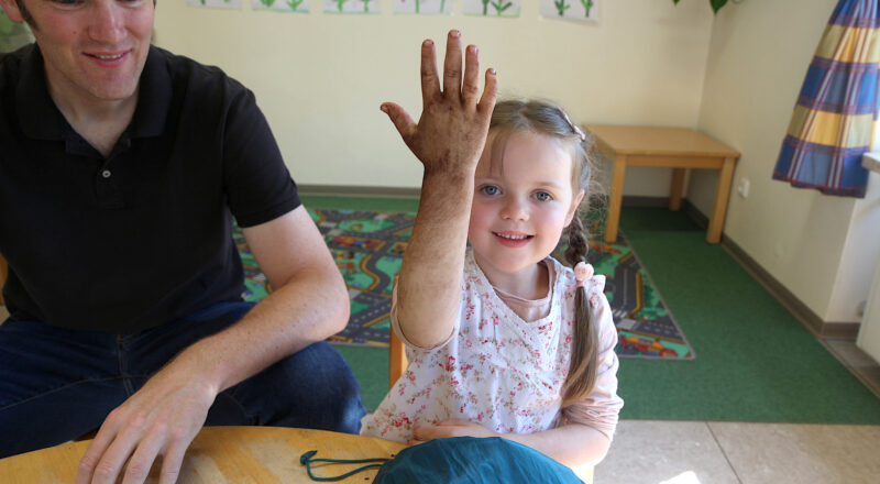 Felice zeigt fröhlich ihre Hand, die beim Durchsuchen des Fühlsacks schmutzig geworden ist. Vater Michael Charton schaut schmunzelnd zu. Foto: Edeltraud Dombert