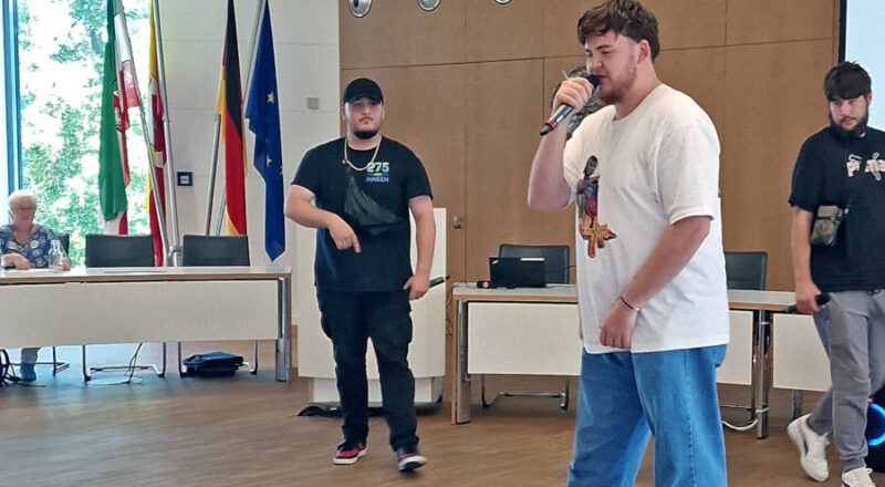 „Rebellion“ im Kreistagssitzungssaal: Almir, Jeremy und Amir (von links) performen ihren Rapsong, der auch von Brigitte van Ahee von den „Omas gegen Rechts“ (hinten links) begeistert verfolgt wurde. Foto: Kreis Lippe