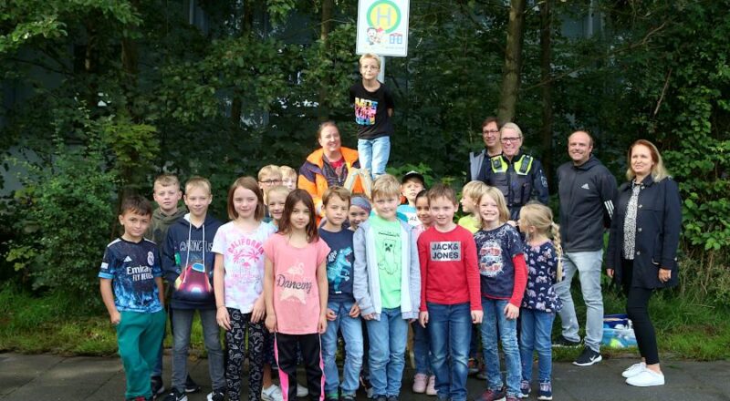 Tim (auf der Leiter) hat gerade das Schild für die Hol- und Bringzone enthüllt. Mit dabei waren seine dritte Klasse, Verkehrsplaner Jens Lehren (neben Tim), Michael Kiszan (vierter von rechts), Polizistin Nina Worm, Frank Sommer (Ordungsbereich Gemeindeverwaltzung) und Schulleiterin Diana Fleeer. Foto: Thomas Dohna