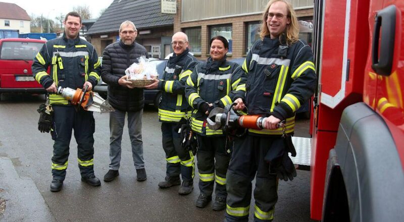 Patrick Reineke (links) trägt einen Spreizer, Dieter Wacker den Präsentkorb. Christopher Dove (rechts) hält eine hydraulische Schere. Reineke, Dove als stellvertretende Zugführer sowie die Zugführer Lars Koppmann und Birgit Niekamp bedankten sich bei Wacker für die seit Jahren gespendeten Fahrzeuge. Foto: Thomas Dohna