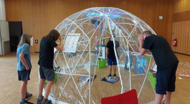 Jugendliche erkunden von innen und von außen das transparente Kuppelzelt in der Ausstellung „Cyberbubble“ und informieren sich zum Thema Fake News. Foto: Stiftung Medien- und Onlinesucht