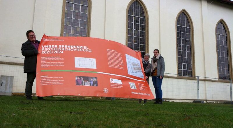 Pfarrer Hendrik Meier, Geschäftsführerin Gundula Huvendiek und Vikarin Mandy Morgenthal halten eines der Plakate, die über die Kirchenrenovierung informieren sollen. Foto: Thomas Dohna