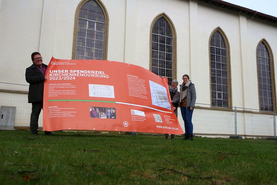 Pfarrer Hendrik Meier, Geschäftsführerin Gundula Huvendiek und Vikarin Mandy Morgenthal halten eines der Plakate, die über die Kirchenrenovierung informieren sollen. Foto: Thomas Dohna