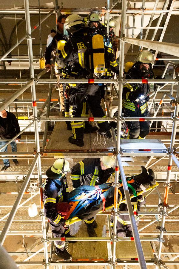 Oben auf dem Gerüst stehen Kräfte unter Atemschutz, unten transportieren Kräfte den "Verletzten" in einer Schleifkorbtrage ab. Foto: Mandy Göhler/Kirchengemeinde Leopoldshöhe