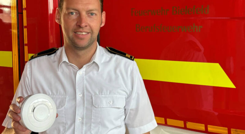 Maximilian Rempe, bei der Feuerwehr Bielefeld zuständig für den Vorbeugenden Brandschutzt, mit einem Rauchmelder. Foto: Stadt Bielefeld