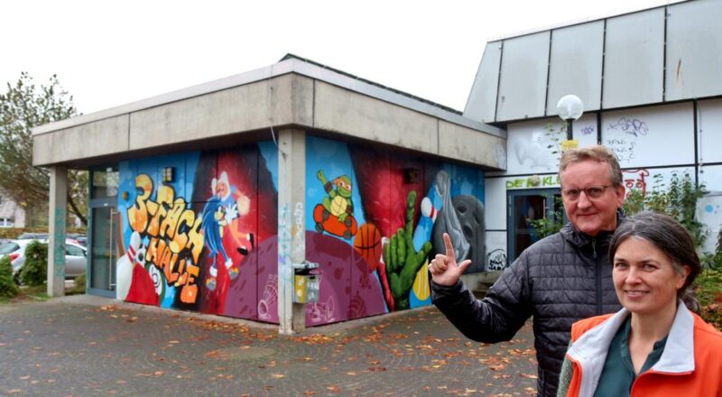 Mathias Pavan zeigt die Handhaltung, die die Jugendlichen an eine Wand an der Dreifachhalle gesprüht haben. Sandra Linnenbecker erläutert das Projekt. Foto: Thomas Dohna