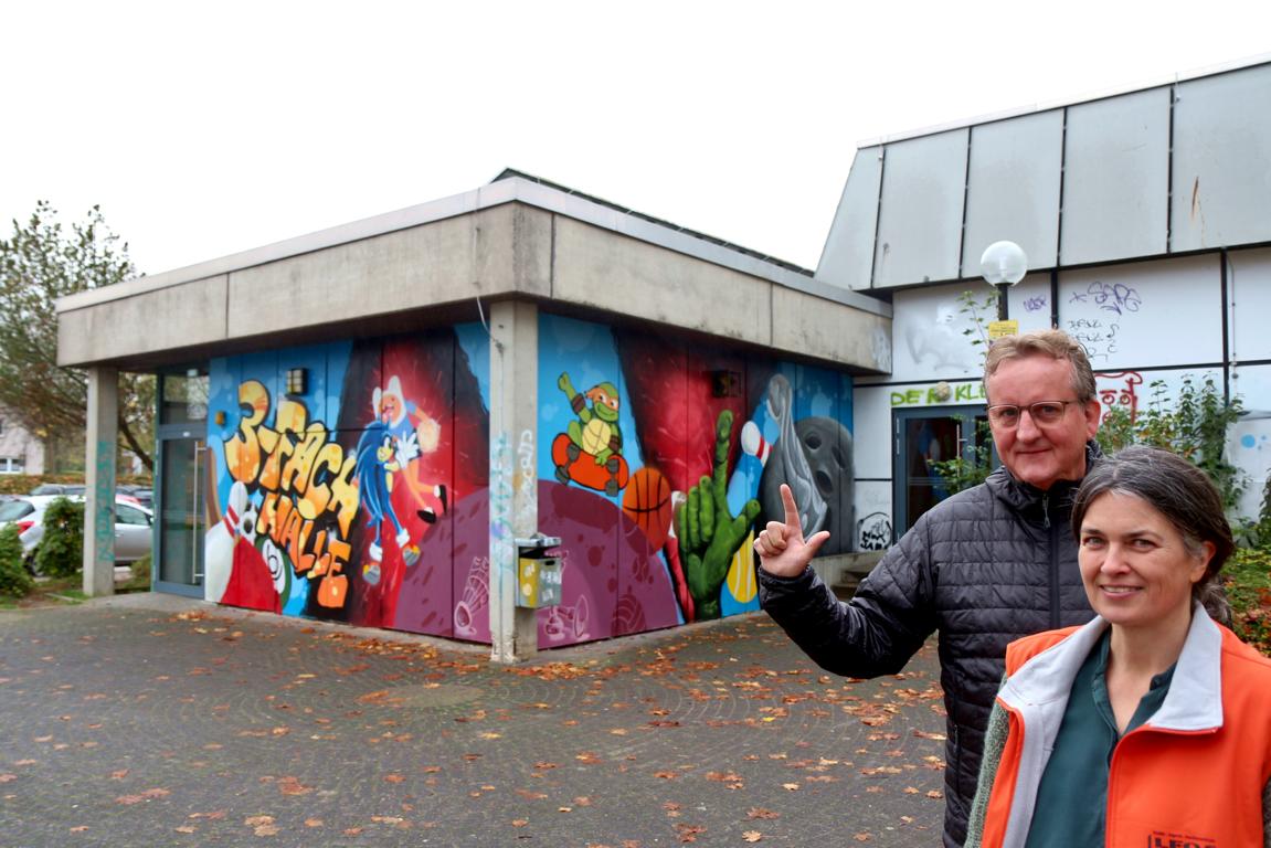 Mathias Pavan zeigt die Handhaltung, die die Jugendlichen an eine Wand an der Dreifachhalle gesprüht haben. Sandra Linnenbecker erläutert das Projekt. Foto: Thomas Dohna