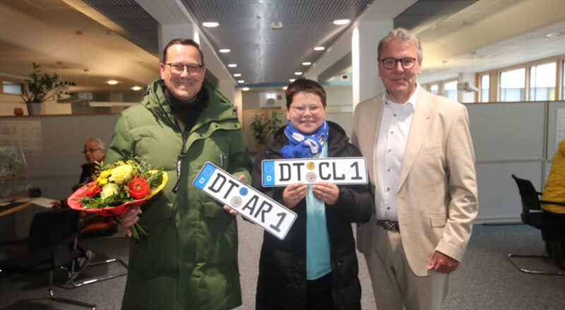 Landrat Meinolf Haase (rechts) beglückwünscht Stefan und Clemens Arlt (von links), die bei der Umkennzeichnungsaktion die Ersten sind, die mit einem neuen DT-Nummernschild die Zulassungsstelle in Detmold verlassen. Foto: Kreis Lippe