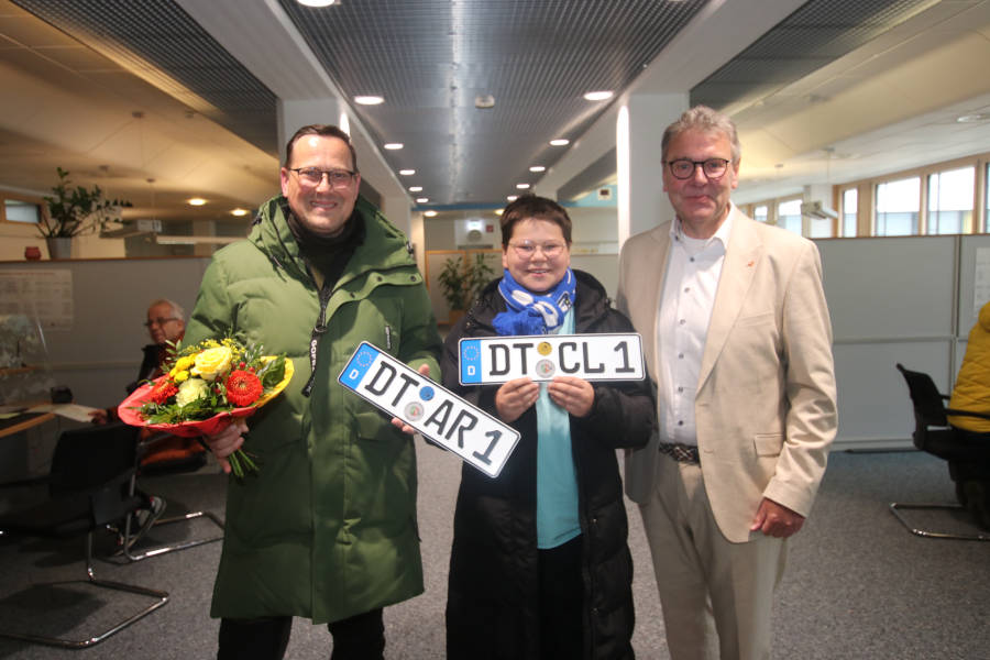 Landrat Meinolf Haase (rechts) beglückwünscht Stefan und Clemens Arlt (von links), die bei der Umkennzeichnungsaktion die Ersten sind, die mit einem neuen DT-Nummernschild die Zulassungsstelle in Detmold verlassen. Foto: Kreis Lippe