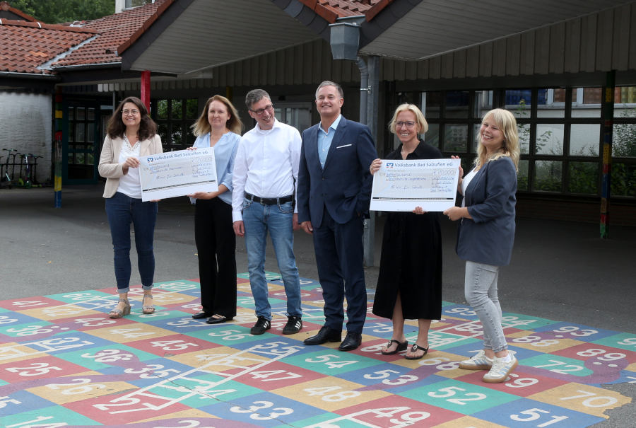 Sandra Fahrenkamp (links) und Isabel Loh (rechts) übergeben die symbolischen Schecks an die Leiterinnen der Grundschule Asemissen Diana Fleer (zweite von links) und der Grundschule Nord Madlen Klarhorst (zweite von rechts). Mit den Schulen freuen sich Bürgermeister Martin Hoffmann (dritter von links) und der Vorstandsvorsitzende der Volksbank Matthia Kruse (dritter von rechts). Foto: Edeltraud Dombert