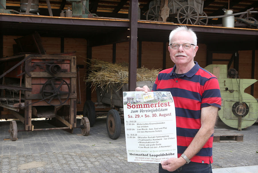 Heimatvereinsvorsitzender Helmut Depping mit dem Plakat zum Programm des Sommerfestes. Im Hintergrund links das neueste Exponat: eine alte Dreschmaschine um 1900. Foto: Edeltraud Dombert