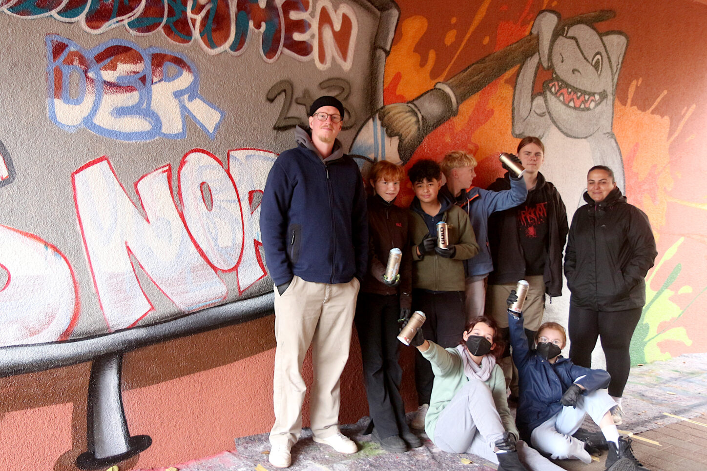 Künstler und Leiter Christoph Cornelius Kollmeier, Marisa Bleymüller, Nilo Asmann, Paul Heuermann, Bufdi Connor Smok, Delstan Khamo vom Familienzentrum Leopoldshöhe,(von links), Marlene Krullmann und Elisa Bleymüller (sitzend von links) arbeiten gemeinsam an der Ausgestaltung des Durchgangs an der Grundschule Nord Foto: Edeltraud Dombert
