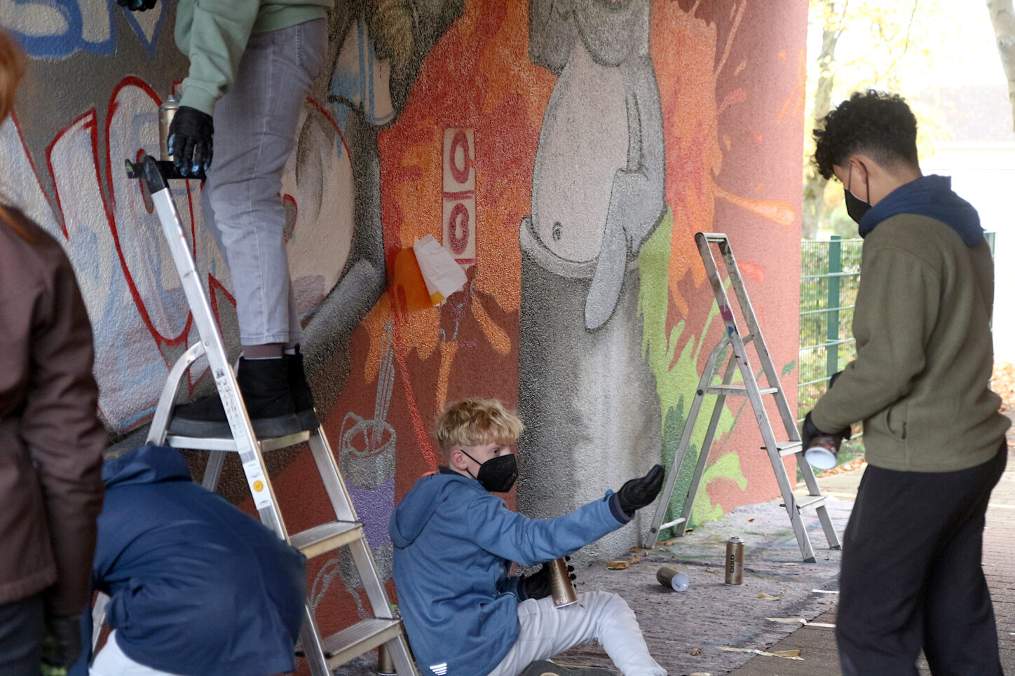 Paul (links) und Nilo arbeiten am unteren Rand des Graffito. Alle schützen sich mit Masken vor den Sprühdämpfen der Farben. Foto: Edeltraud Dombert